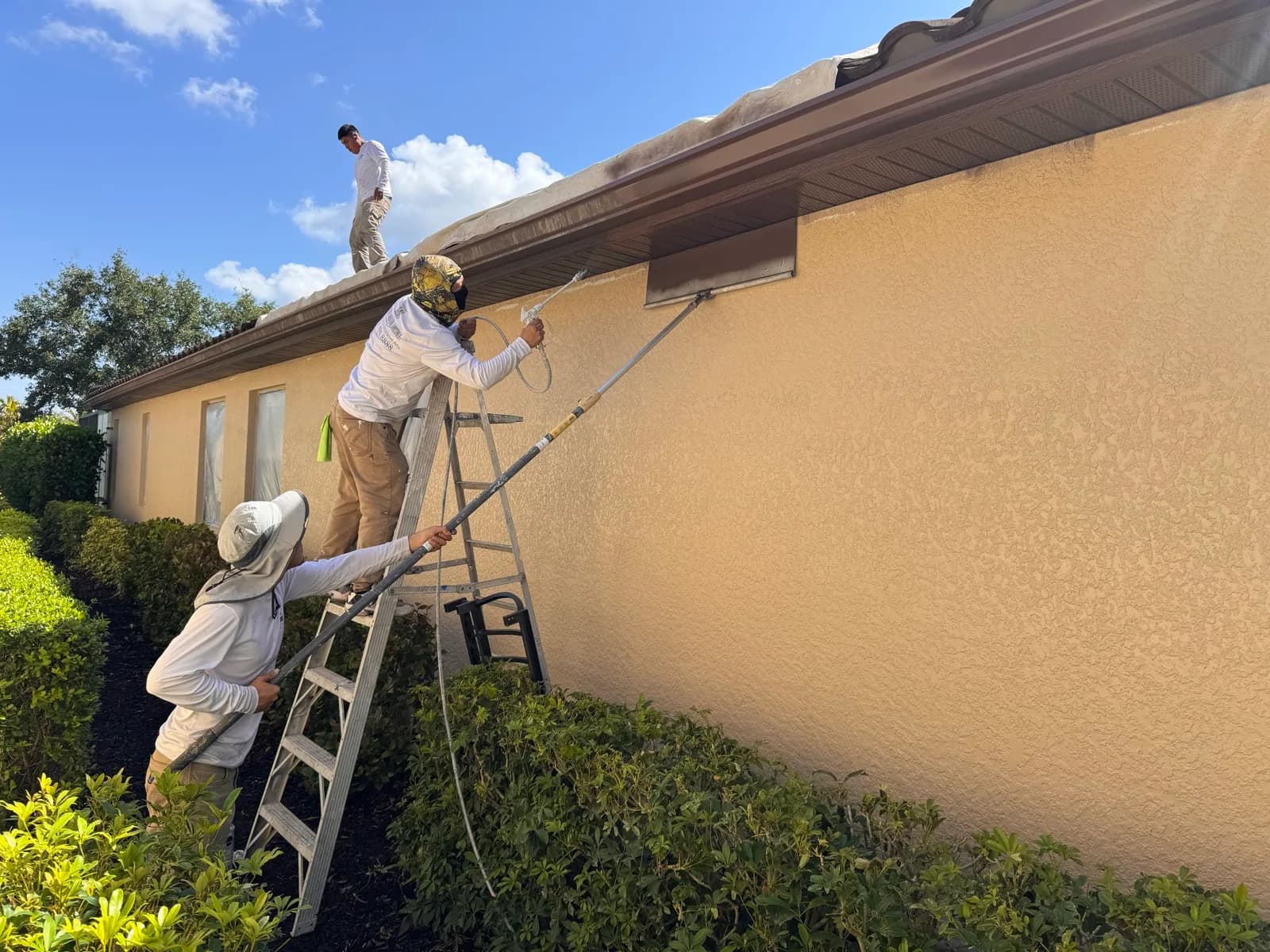 Crew rolling coating onto a stucco wall from ladders