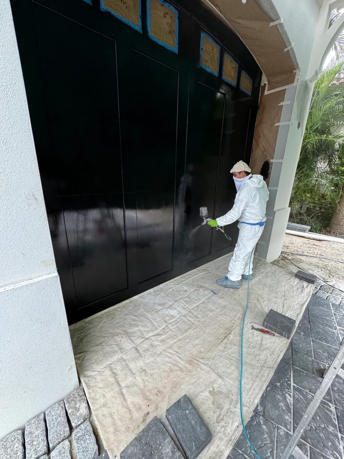 Crew member spraying a garage door under full masking